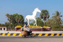Hombre y mujer montando en carretera rotonda con estatua de caballo, Kep, Camboya - foto de stock