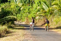 Deux hommes faisant du vélo à travers la rue à Madagascar, Afrique — Photo de stock