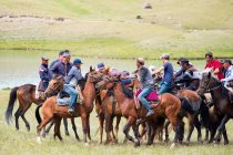 Región OSH, KYRGYZSTAN - 22 de julio de 2017: Nomadgames, men on horses, lake on background - foto de stock