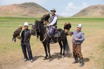 AK SAY, ISSYK-KUL REGION, KYRGYZSTAN - AUGUST 12, 2017: Eagle hunters with golden eagles, mountain landscape on background — Stock Photo