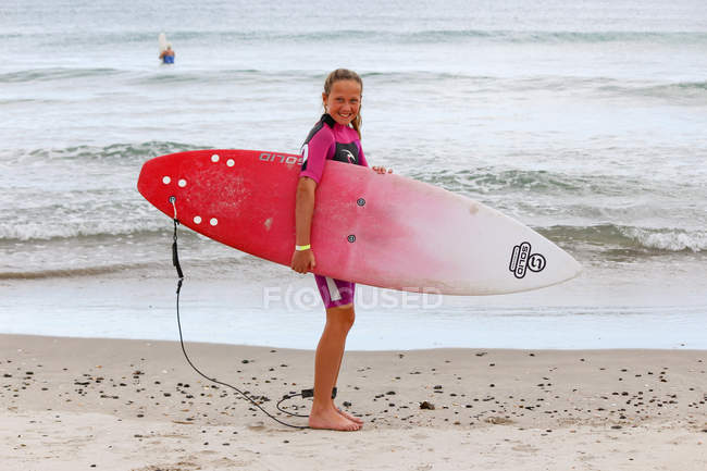 Chica de pie en la playa con tabla de surf, Northland, Nueva Zelanda - foto de stock