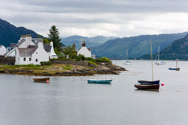 Reino Unido, Escocia, Highland, Plockton, Plockton, asentamiento en las Highlands, vista panorámica del lago con barcos y pueblos a orillas, montañas en el fondo - foto de stock