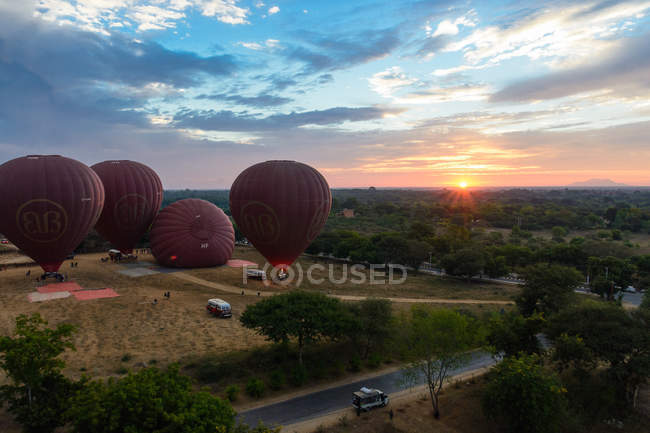 Мьянма (Бирма), Мандалайская область, Старый Баган, Воздушные шары над Баганом, автомобили, припаркованные у поля на солнце — стоковое фото
