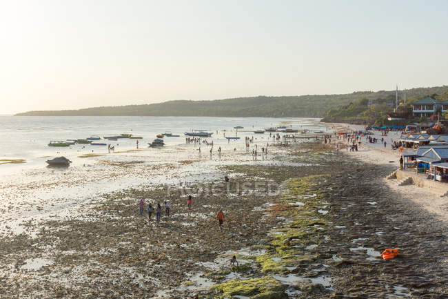 Indonesia, Sulawesi Selatan, Bulukumba, Beach of Bira, walking people, boats and residential buildings by the shore in sunset light — Stock Photo