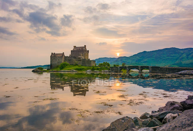 Reino Unido, Escocia, Highland, Dornie, Loch Duich, Eilean Donan Castle by lake at scenic sunset - foto de stock