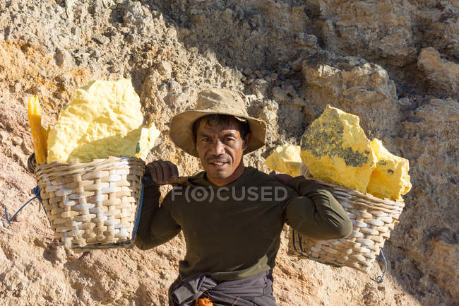 JAVA, INDONESIA - 18 DE JUNIO DE 2018: Minería de azufre en el volcán Ijen, hombre portando azufre en canastas por cráter - foto de stock