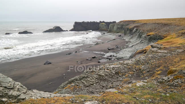 Ebbe am schwarzen Sandstrand mit Klippen, Island — Stockfoto