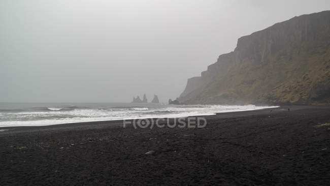 Playa de arena negra con rocas cubiertas de niebla, Islandia, Myrdalshreppur - foto de stock
