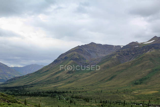 Canada, Yukon Territory, Yukon, On the Dampster Highway Juzgando el paisaje salvaje del norte con montañas bajo el cielo pesado - foto de stock