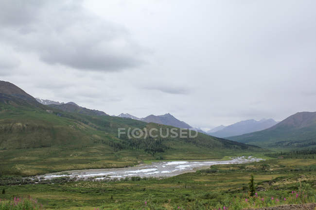 Canada, Territoire du Yukon, Yukon, Sur la route Dampster Juger le paysage sauvage du Nord avec des montagnes et une rivière sous un ciel lourd — Photo de stock