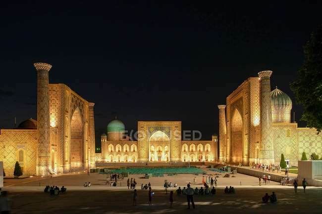 Узбекистан, Самарканд, Самарканд, люди, що йдуть на площі, медресе освітлені вночі — стокове фото