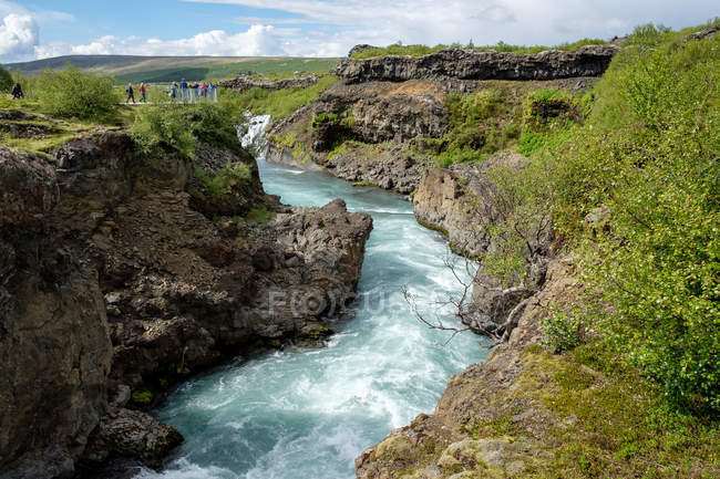 Distant view of tourists on cliffs by river, Iceland — Stock Photo