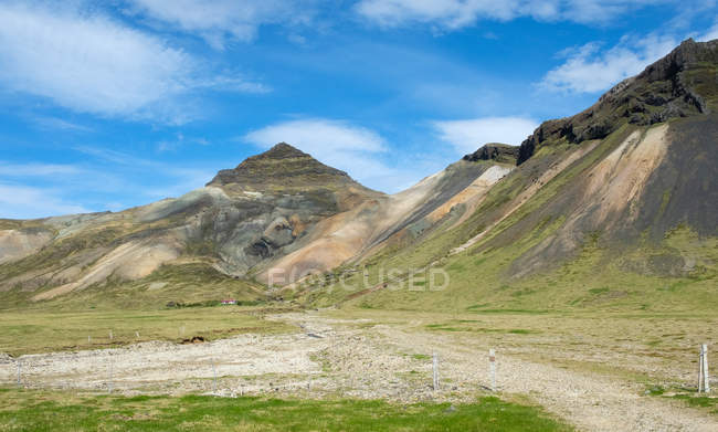 Route de terre et rochers sous un ciel nuageux bleu, Islande — Photo de stock