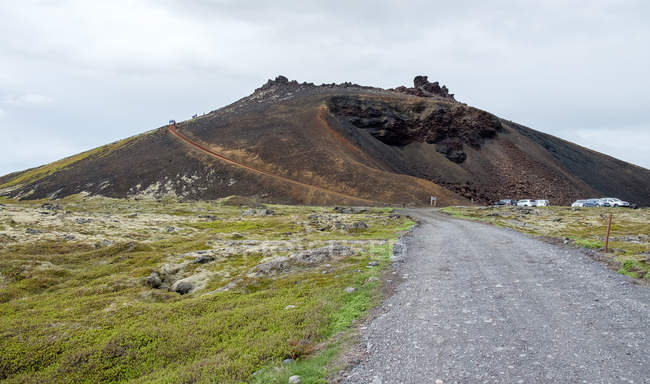 Saxholl Cráter de escoria y coches aparcados bajo el cielo nublado, Islandia - foto de stock