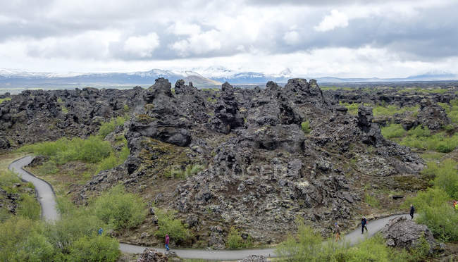 Turistas lejanos y estructuras de lava bajo el cielo nublado, Islandia, Dimmuborgir - foto de stock