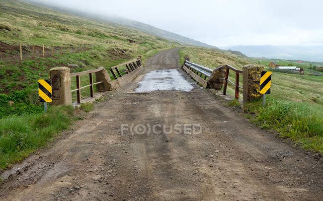Dirt road with small bridge and distant foggy landscape, Iceland — Stock Photo