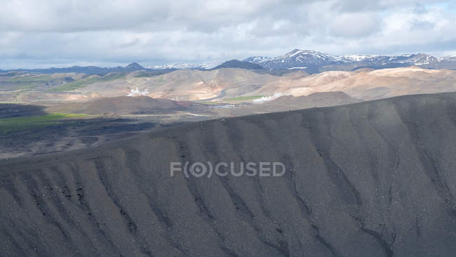 Part of crater Hverfjall and mountainous landscape under cloudy sky — Stock Photo