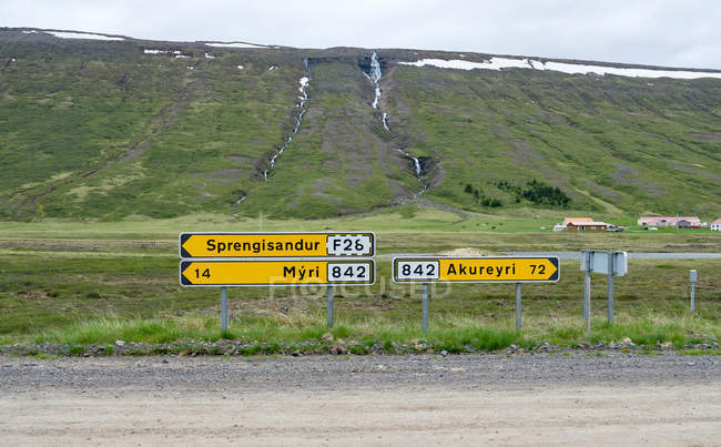 Yellow direction signs with green hill on background, Iceland — Stock Photo