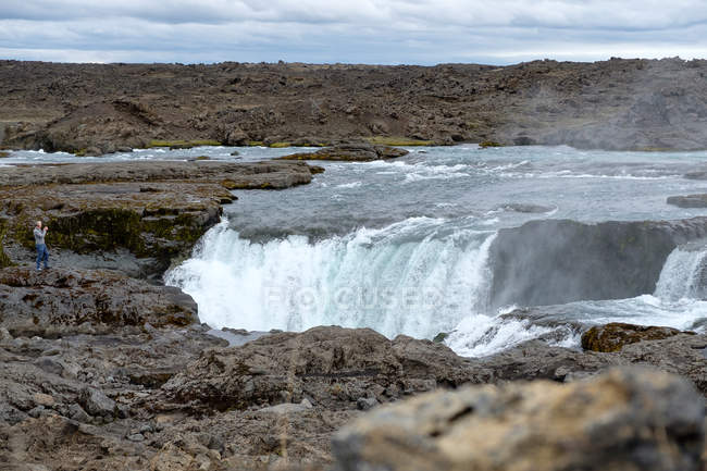 Lontano turista fotografare cascata Hrafnahjargafoss, Islanda — Foto stock