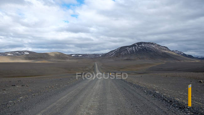 Dirt road with distant mountains under cloudy sky, Iceland — Stock Photo