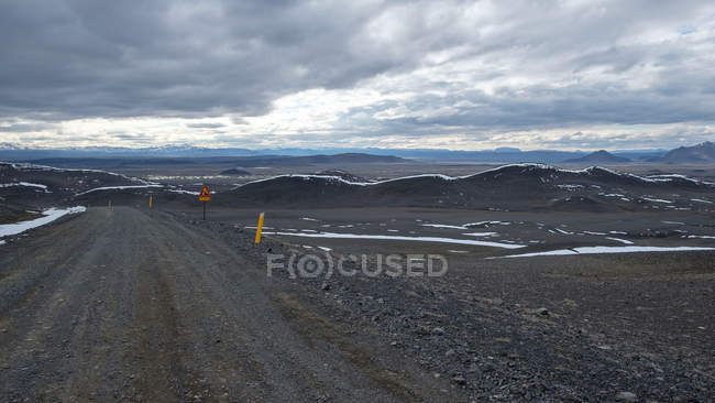 Strada sterrata con montagne lontane sotto cielo nuvoloso, Islanda — Foto stock
