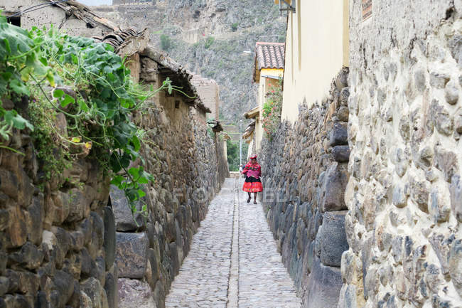 Vista posteriore della donna locale che cammina in uno stretto vicolo di vecchi edifici in pietra a Ollantaytambo, Qosqo, Perù . — Foto stock