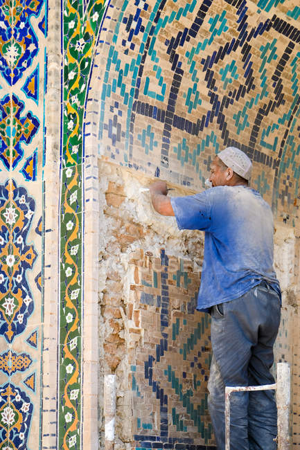 MADRASA EN REGÍSTRATE, SAMARKAND, UZBEKISTÁN - 6 DE JUNIO DE 2017: Hombre trabajando en la renovación de azulejos de la pared en madrasa - foto de stock