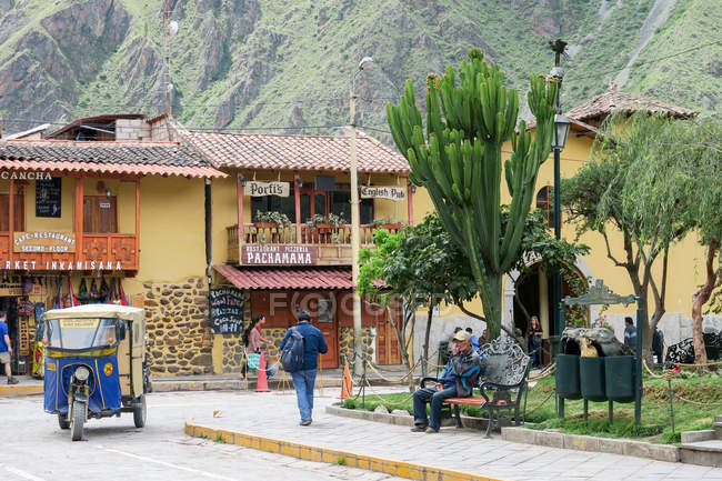 Paisajes callejeros con gente local, vehículo tuk tuk, casas tradicionales y carteles y plantas suculentas que crecen en la ciudad de Ollantaytambo, Qosqo, Perú . - foto de stock