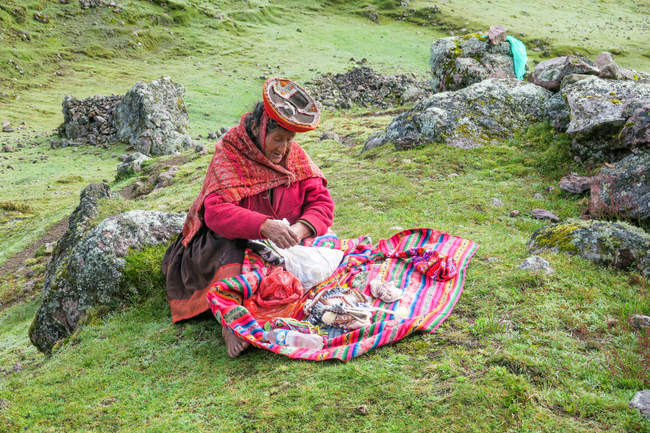 Frau in Nationalkleidung sitzt auf felsigem Hügel, lares, cuzco, peru — Stockfoto
