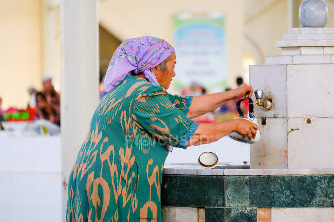 Vieille femme versant de l'eau dans une bouilloire dans un grand bazar, Buxoro, Ouzbékistan — Photo de stock