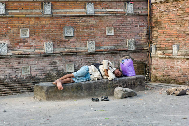 Paisagem de rua com o homem adormecido no banco de pedra em Yogyakarta, Java, Indonésia, Ásia — Fotografia de Stock