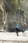 Young woman swinging on rope at Mystic Beach along Juan de Fuca Trail, Vancouver Island, Canada — Stock Photo