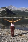 Mujer practicando yoga a lo largo de la orilla de Spray Lakes, Kananaskis Country, Alberta, Canadá . - foto de stock