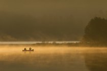 Zwei Männer paddeln Kanu bei Sonnenaufgang auf dem Ochsenzungensee, Muskoka, Ontario, Kanada. — Stockfoto