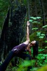 Asian woman practicing yoga triangle posture near Clearwater River, Clearwater, British Columbia, Canada — Stock Photo