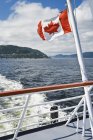 Bandiera canadese a poppa di navigazione sul fiume Saguenay, Pointe-Noire in Baie-Sainte-Catherine, Charlevoix, Quebec, Canada — Foto stock