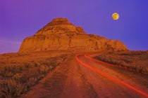 Luces de cola en la carretera con Castle Butte rock en Big Muddy Badlands, Saskatchewan, Canadá - foto de stock