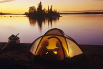 Siluetas de pareja acampando en tienda de campaña en Otter Falls, Whiteshell Provincial Park, Manitoba, Canadá . - foto de stock