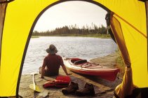 Rear view of male tourist resting along Whiteshell River, Whiteshell Provincial Park, Manitoba, Canada. — Stock Photo