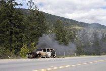 Voiture en feu sur le côté de la route dans les bois du Canada . — Photo de stock