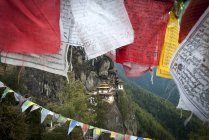 Banderas de oración y Taktsang Tigers Nest Monasterio en rocas sobre Paro, Bután - foto de stock