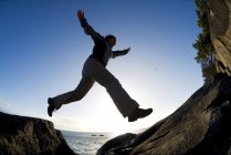 Low angle view of female hiker jumping on rocks, East Sooke Regional Park, Victoria, British Columbia, Canada. — Stock Photo