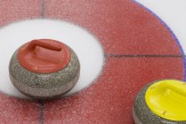 Nahaufnahme von roten und gelben Curlingsteinen auf Eis. — Stockfoto