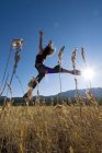 Dançarina saltando em campo gramado com sol brilhando, Lago Tatlayoko, Colúmbia Britânica, Canadá . — Fotografia de Stock