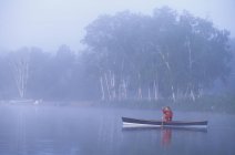 Young woman canoeing in early morning mist, Oxtongue Lake, Muskoka, Ontario, Canada. — Stock Photo