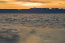 Sailboats appearing in ocean covered with fog and clouds with sun setting behing mountains, British Columbia, Canada. — Stock Photo
