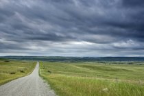 Route de campagne à travers champ et clôture sous des nuages orageux près de Cochrane, Alberta, Canada — Photo de stock