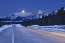 Route hivernale et lune dans le ciel à Bighorn Wildland, Alberta, Canada — Photo de stock