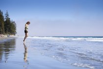 Young woman stepping into ocean water at China Beach in Juan de Fuca Provincal Park, Vancouver Island, Canada. — Stock Photo