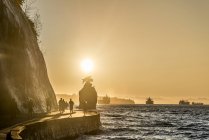 Silhouetten von Menschen, die bei Sonnenuntergang auf der Strandpromenade des Stanley Parks flanieren, Vancouver, britische Kolumbia, Kanada — Stockfoto
